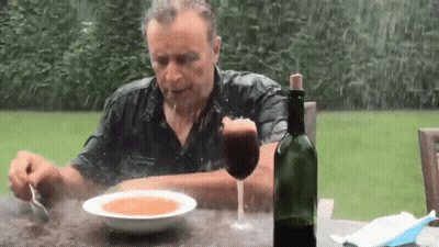 A Man Is Sitting At A Table Eating Soup And Drinking Wine GIF