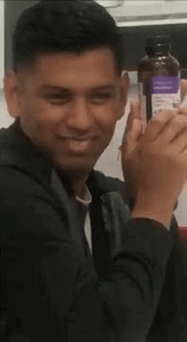 A Man Is Sitting At A Table Holding A Bottle Of Alcohol . GIF