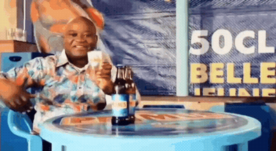 A Man Is Sitting At A Table Holding A Bottle Of Beer And A Glass Of Beer . GIF