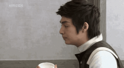 A Man Is Sitting At A Table Holding A Cup Of Coffee In His Hand . GIF