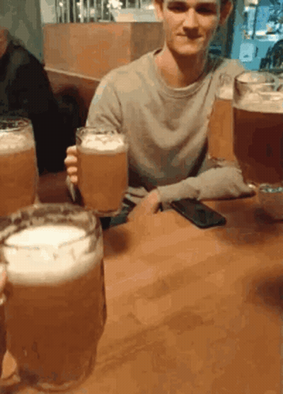 A Man Is Sitting At A Table Holding A Glass Of Beer And A Phone GIF