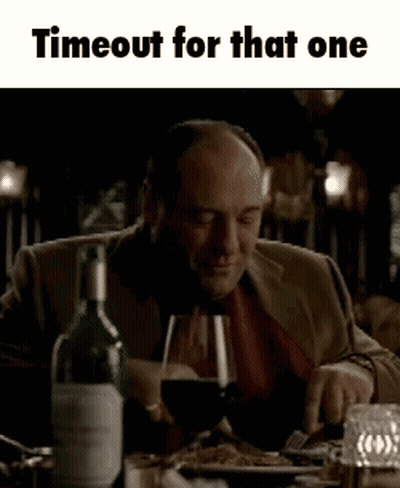 A Man Is Sitting At A Table Holding A Glass Of Wine . GIF