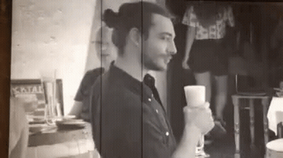 A Man Is Sitting At A Table Holding A Glass Of Wine In A Black And White Photo . GIF