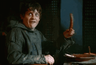 A Man Is Sitting At A Table Holding A Sausage And Making A Funny Face . GIF