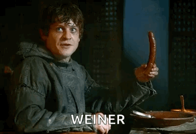 A Man Is Sitting At A Table Holding A Sausage And The Word Weiner Is Visible . GIF