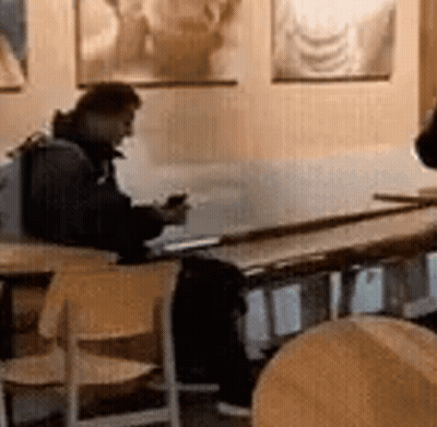 A Man Is Sitting At A Table In A Restaurant Looking At His Phone GIF