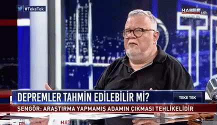A Man Is Sitting At A Table In Front Of A Sign That Says " Depremler Tahmin Edilebilir Mi " GIF