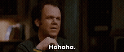 A Man Is Sitting At A Table Laughing While Holding His Hand To His Chin . GIF