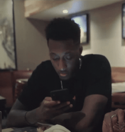A Man Is Sitting At A Table Looking At His Cell Phone GIF