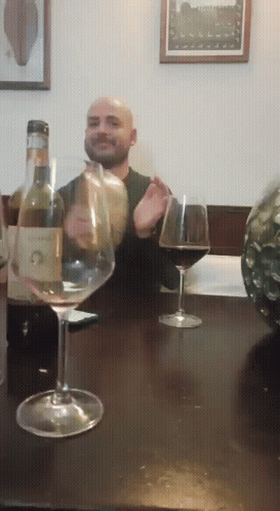A Man Is Sitting At A Table With A Bottle Of Wine And A Glass Of Wine GIF