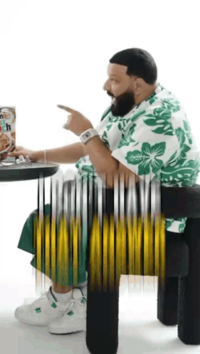 A Man Is Sitting At A Table With A Box Of Cereal In Front Of Him And Pointing At It . GIF