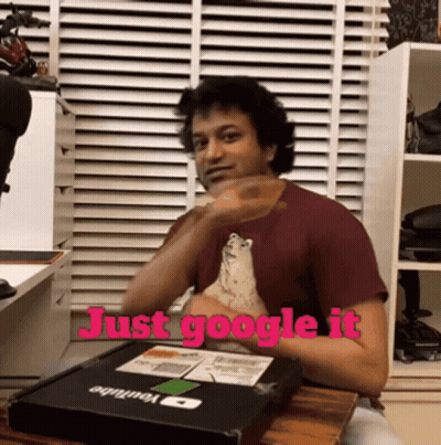 A Man Is Sitting At A Table With A Box That Says Just Google It GIF