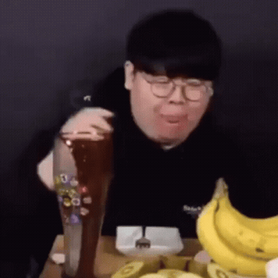 A Man Is Sitting At A Table With A Bunch Of Bananas And A Glass Of Beer . GIF