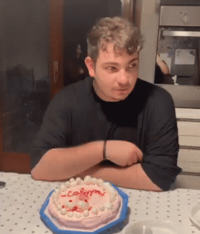 A Man Is Sitting At A Table With A Cake On It And Looking At It . GIF
