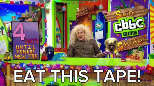 A Man Is Sitting At A Table With A Dog And A Sign That Says Eat This Tape GIF