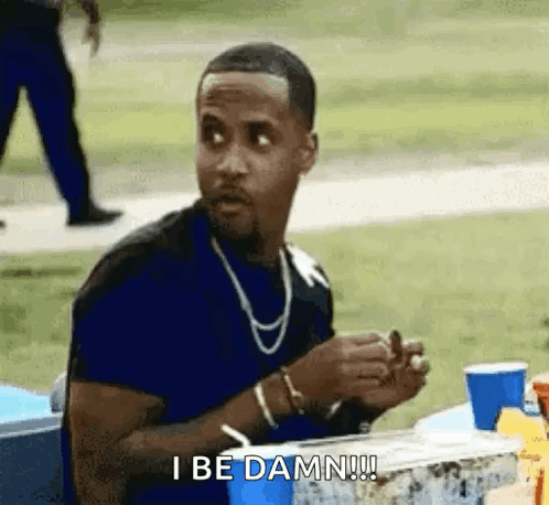 A Man Is Sitting At A Table With A Drink And A Cigarette In His Hand . GIF
