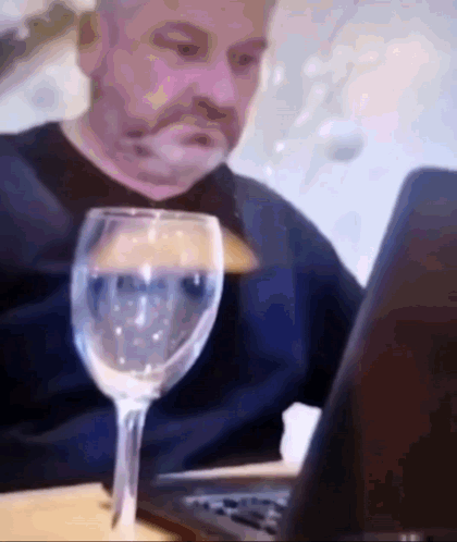 A Man Is Sitting At A Table With A Glass Of Water And A Laptop . GIF