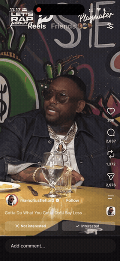 A Man Is Sitting At A Table With A Glass Of Water In Front Of A Sign That Says Playmaker GIF