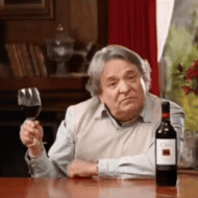 A Man Is Sitting At A Table With A Glass Of Wine And A Bottle Of Wine . GIF