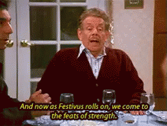 A Man Is Sitting At A Table With A Glass Of Wine And Says And Now As Festivus Rolls On We Come GIF