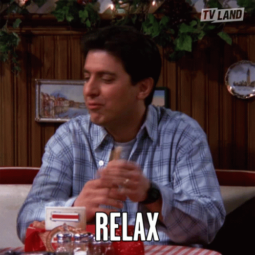 A Man Is Sitting At A Table With A Glass Of Wine And The Word Relax Is On The Table GIF