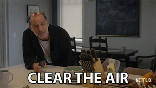 A Man Is Sitting At A Table With A Knife Holder And A Sign That Says Clear The Air GIF
