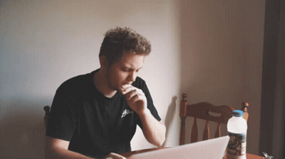 A Man Is Sitting At A Table With A Laptop And A Bottle Of Water GIF