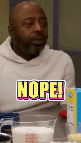 A Man Is Sitting At A Table With A Measuring Cup Of Milk And A Sticker That Says Nope GIF