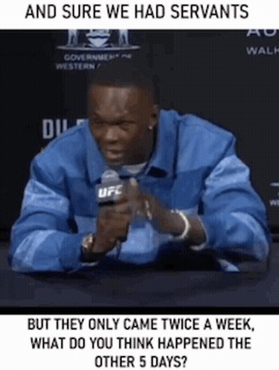 A Man Is Sitting At A Table With A Microphone In His Hand And Talking Into It . GIF