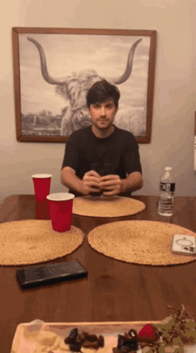 A Man Is Sitting At A Table With A Picture Of A Bull On The Wall Behind Him GIF