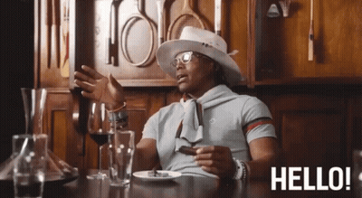 A Man Is Sitting At A Table With A Plate Of Food And A Glass Of Wine And The Words Hello Behind Him GIF