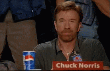 A Man Is Sitting At A Table With A Sign That Says Chuck Norris GIF