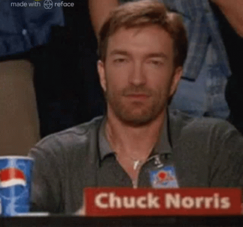A Man Is Sitting At A Table With A Sign That Says Chuck Norris On It . GIF