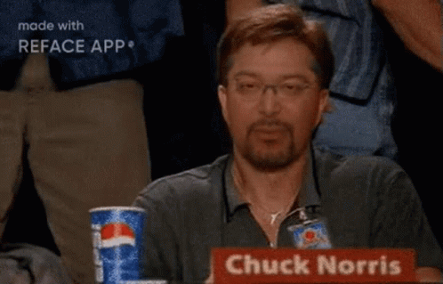 A Man Is Sitting At A Table With A Sign That Says Chuck Norris On It GIF