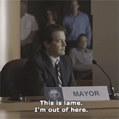 A Man Is Sitting At A Table With A Sign That Says Mayor On It GIF
