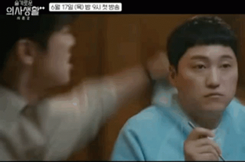 A Man Is Sitting At A Table With Chopsticks In His Hand And Another Man Is Standing Next To Him . GIF
