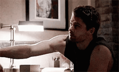 A Man Is Sitting At A Table With His Arm Outstretched In Front Of A Lamp . GIF