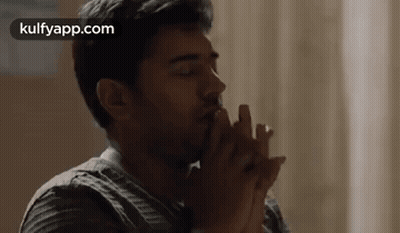 A Man Is Sitting At A Table With His Hands Folded In Front Of His Face . GIF