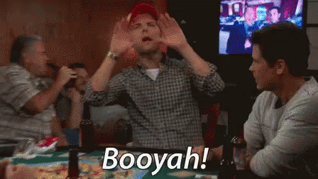 A Man Is Sitting At A Table With His Hands In The Air And The Words Booyah On The Screen . GIF