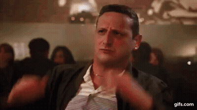 A Man Is Sitting At A Table With His Hands On His Chest In A Crowded Room . GIF