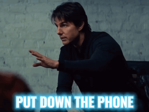 A Man Is Sitting At A Table With The Words Put Down The Phone Above Him GIF