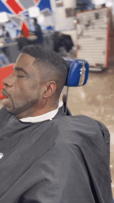A Man Is Sitting In A Barber Chair With His Eyes Closed . GIF