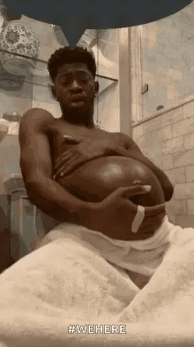 A Man Is Sitting In A Bathroom With A Towel Around His Waist And Holding His Belly . GIF