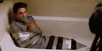 A Man Is Sitting In A Bathtub With Tape On His Mouth . GIF