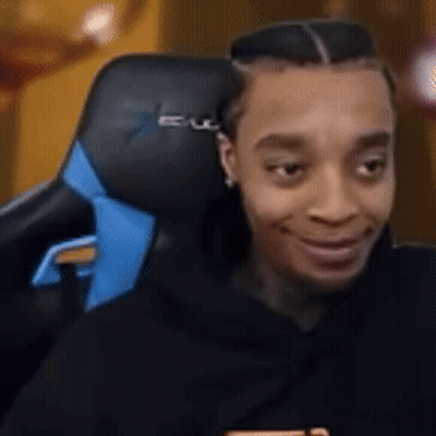 A Man Is Sitting In A Black And Blue Gaming Chair . GIF