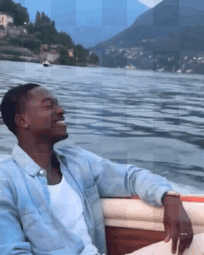 A Man Is Sitting In A Boat On A Lake GIF
