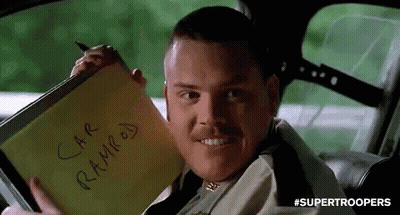 A Man Is Sitting In A Car Holding A Notepad That Says `` Car Ramped '' On It . GIF