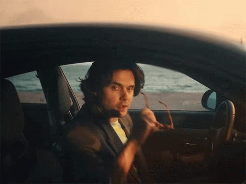 A Man Is Sitting In A Car Holding A Pair Of Sunglasses GIF