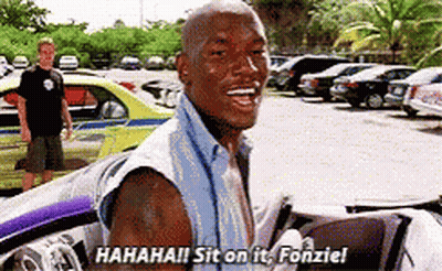 A Man Is Sitting In A Car In A Parking Lot And Laughing While A Man Stands In The Background . GIF