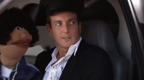 A Man Is Sitting In A Car Next To A Puppet . GIF